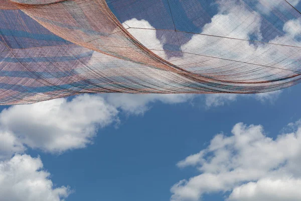 Draped shade cloth high in the air against a blue sky with clouds, creative copy space, horizontal aspect