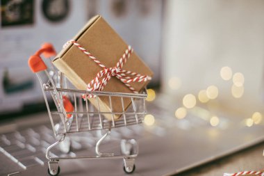 Masasında dizüstü bilgisayarı olan minyatür alışveriş arabası. Çevrimiçi alışveriş kavramı. Yakın plan.