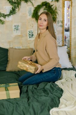 Güzel bir kadın süslü bir yatak odasında elinde Noel hediyesi ya da hediyesiyle oturuyor. Tatil kavramı
