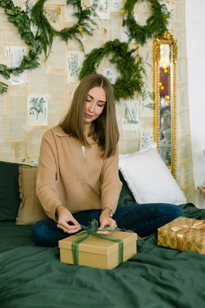 Süslü yatak odasında, paketlenmiş Noel hediyesi ya da hediyeyle yatakta oturan mutlu bir kadın. Tatil kavramı