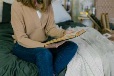 Rahat, beyaz bir kadın, günlük kıyafet kitaplarıyla evde rahat bir şekilde yatağında, dekore edilmiş yatak odasında dinleniyor. Mutlu Kış Noel Tatilleri
