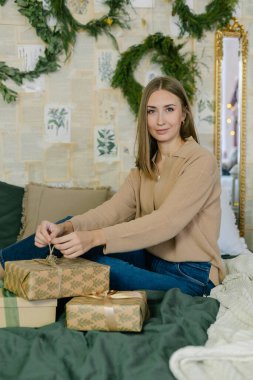 Noel ya da yeni yıl tatili için hazırlık kavramı. Çekici genç bir kadın evde yatağında oturuyor, ailesi ve arkadaşları için hediyeler hazırlıyor.
