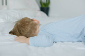 Roztomilý chlapeček v modrém pyžamu spí doma v posteli