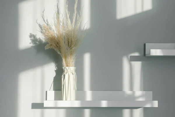 Home interior floral decor. Dried flowers in vase on white shelf. Background with shadow lights. Still life, Minimal concept