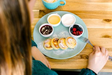 Kahvaltı yapan genç bir kadın. Kafedeki ahşap masada süzme peynirli krep ve kapuçino. Üst görünüm