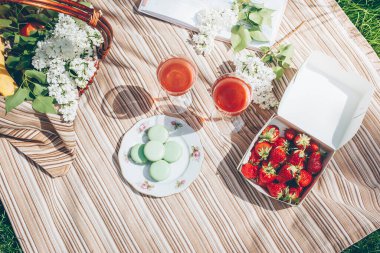 Yaz pikniğinde. Çilek, badem kurabiyesi, içecek ve çiçekli sepet beyaz leylak. Üst manzara, düz uzanma