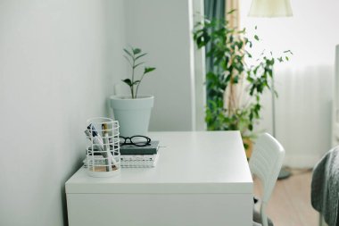 Evdeki modern ofis masası. Çalışma odası, defter, ofis malzemeleri, gözlük, ev bitkisi. İçerisi aydınlık. Boşluğu kopyala