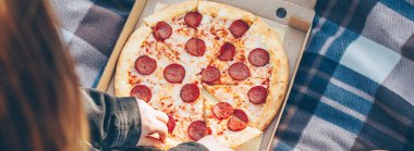 Doğada piknikte otururken lezzetli biberli pizza yiyen bir kız. Üst görünüm