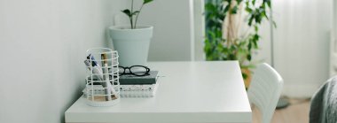 Evdeki modern ofis masası. Çalışma odası, defter, ofis malzemeleri, gözlük, ev bitkisi. İçerisi aydınlık. Boşluğu kopyala
