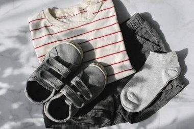 Çizgili tişört, gri şort, arka planda spor ayakkabı. Üst manzara, düz uzanma