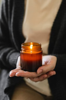 Woman holding in hand burning candle in small amber glass jar with wooden wick. Zen and relax concept.