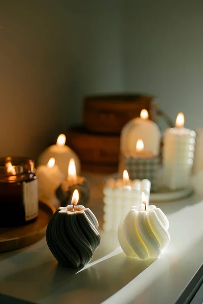 Cozy burning candles on white shelf. Concept of winter or autumn home interior decor