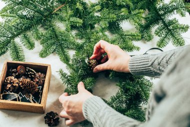 Woman in gray knitted sweater making a christmas fir wreath. Christmas decorating for home interior. Step by step, process. DIY, crafting, hobby concept