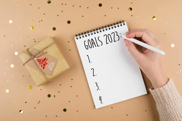 New Year goals 2023. Woman\'s hand writing in note pad goals list. Concept of new year planning. Top view, copy space. Place for text