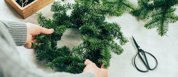 Woman making a christmas fir wreath. Christmas decorating for home interior. Long banner image for design
