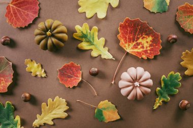 Kahverengi arka planda balkabağı ve sonbahar yaprakları şeklinde iki mum. Sonbahar mevsimi konsepti