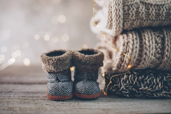 Stack of cozy winter knitted sweaters, cute small boots and christmas ornaments on a blurred background with bokeh. Warm Cozy Concept. Copy space