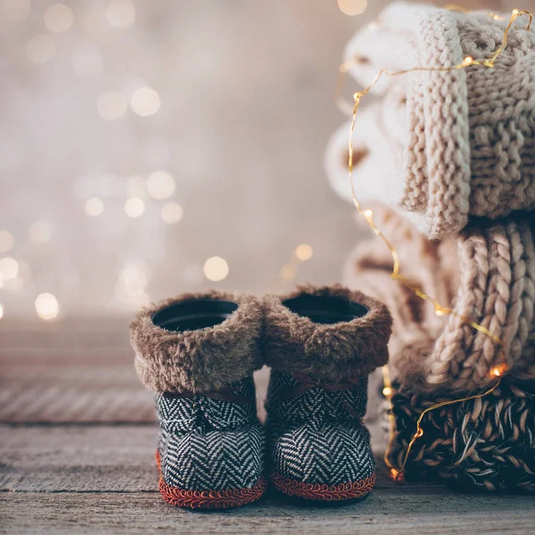 Stack of cozy winter knitted sweaters, cute small boots and christmas ornaments on a blurred background with bokeh. Warm Cozy Concept. Copy space.