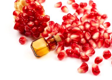 Nar yağı ve dağınık nar tohumları beyaz arka planda izole edilmiş. Kırmızı punica granatum esaslı yağ, tentür, özüt, infüzyon, uçucu yağlar, özü