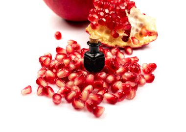 Nar yağı ve dağınık nar tohumları beyaz arka planda izole edilmiş. Kırmızı punica granatum esaslı yağ, tentür, özüt, infüzyon, uçucu yağlar, özü