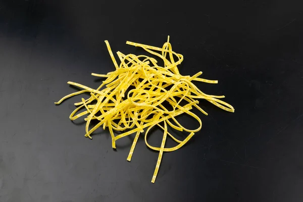 生の黄色のイタリアのタグリアテッレパスタ 卵自家製ドライリボンヌードル 薄いマカロニリボン 黒の背景に短い調理されたスパゲティトップビュー — ストック写真