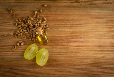 Küçük şarap şişesinde üzüm yağı tohumu. Yeşil dilimli bir yığın üzüm tohumu ve temel yağ, tentür, özü, ahşap kırsal arkaplan manzarası üzerine dökülen fotokopi alanı manzarası.