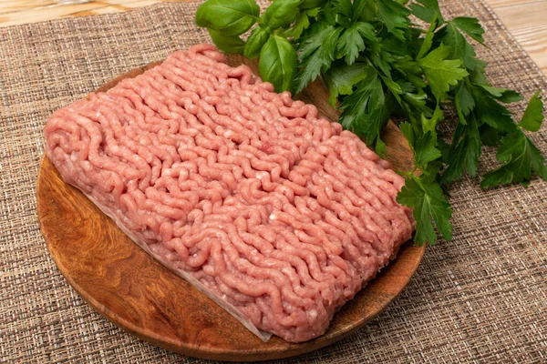 Turkey minced meat. Ground fillet on wood plate, uncooked turkey mincemeat, raw forcemeat, fresh farce meat portion with greens