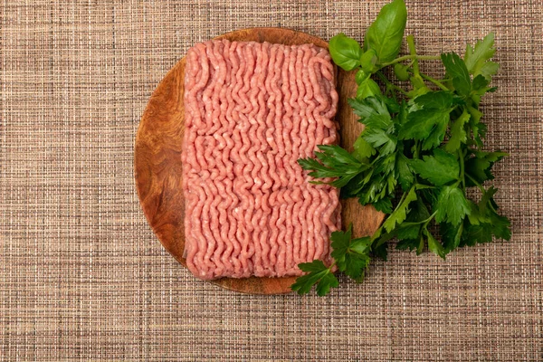 Turkey minced meat. Ground fillet on wood plate, uncooked turkey mincemeat, raw forcemeat, fresh farce meat portion with greens top view