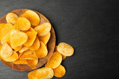 Patates cipsleri yakın plan karanlık taş üzerine yığılır. Çıtır çıtır patates çerez yığını, yeşillikli fast food atıştırmalıkları, baharatlar, kırmızı biber tozu.
