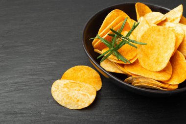 Patates cipsleri siyah kaseye yığılır. Arka planda koyu taşla yakın plan çekimde. Çıtır çıtır patates çerez yığını, yeşil, baharatlı fast food atıştırmalıkları, kırmızı biber tozu.