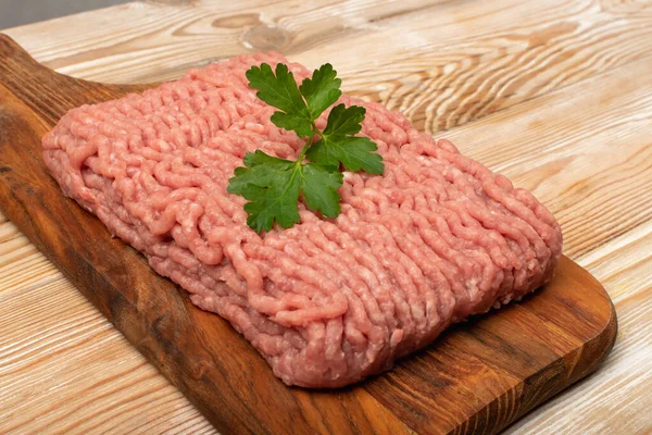 Turkey minced meat. Ground fillet on wood background, uncooked turkey mincemeat, raw forcemeat, fresh farce meat portion with greens