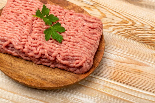 Turkey minced meat. Ground fillet on wood plate background, uncooked turkey mincemeat, raw forcemeat, fresh farce meat portion with greens