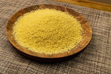 Couscous pile on wood plate closeup. Dry cuscus, raw kuskus, uncooked cous cous or semolina granules on rustic background