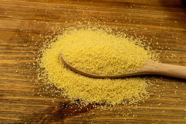 Kuskus yığını yakın çekim. Tahta kaşıkta kuru yastık, çiğ kuskus, pişmemiş kuskus veya ahşap arka planda irmik granüller.