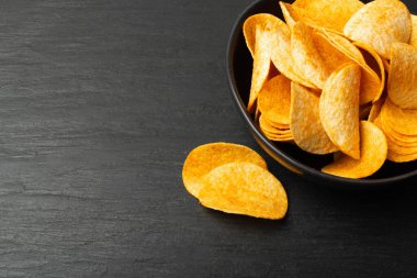 Patates cipsleri siyah kaseye yığılır. Arka planda koyu taşla yakın plan çekimde. Çıtır çıtır patates çerez yığını, yeşil, baharatlı fast food atıştırmalıkları, kırmızı biber tozu.