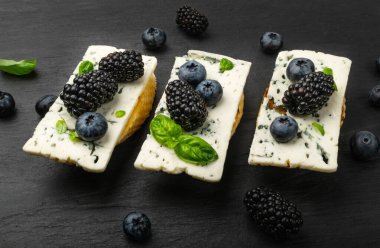 Ekmeğin üstünde mavi peynir. Böğürtlen ve bal ile Gorgonzola, ricotta ile bruschetta, yaban mersini ve böğürtlen, siyah taş arka planda Fransız tostu.