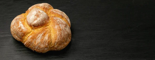 Homemade braided bread on black stone background. Round rustic loaf, traditional bread top view with copy space