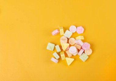 Sarı arka planda tablet şekerler. Sıkıştırılmış şeker tozu şekerlemesi, dekstroz şeker kolye parçaları, C vitamini tabletleri, pastiller üst görünüm yığını