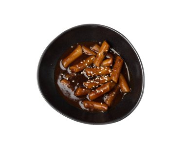 Siyah kasede sade bir içki. Topokki Kore yemeği, pirinç keki çubukları, tukbokki, beyaz arka planda pişmemiş tteokbokki.