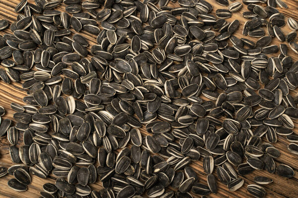 Sunflower seeds texture background. Raw sunflower seed pattern, sun flower grains on wooden rustic table desk, fresh edible striped oil seeds flat lay, top view with copy space