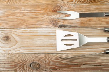 Ahşap arka planda ızgara aletleri ayarlandı. BBQ metal ekipmanları, çelik barbekü çatalı, tong, ahşap masa zemininde fotokopi alanı olan spatula