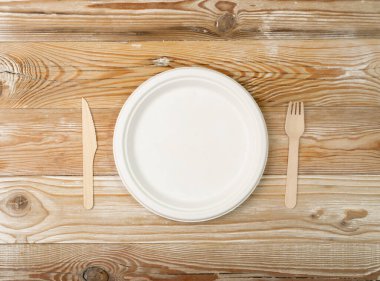 Kağıt tabak, çatal, tahta masada bıçak. Eko sofra takımı, tek kullanımlık çatal bıçak, biyolojik çözünürlük, piknik için eko biyo tablo ayarı, geri dönüşümlü gereçleri beyaz arka plan görünümünde kopyalama alanı ile yeniden kullanılabilir hale getir