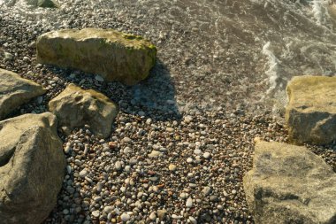Sea waves on pebble beach texture background. Transparent ocean water, rocky shore pattern, summer mockup with copy space, stone shoreline, vacation concept