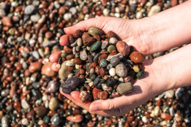 Colored pebble beach in hands. Multicolored rocky shore pattern, summer mockup with copy space, stone handful, vacation concept