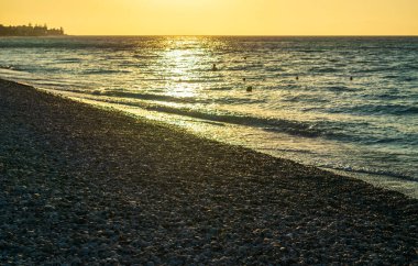 Sea waves on pebble beach texture background on sunset. Transparent ocean water, rocky shore pattern, summer mockup with copy space, stone shoreline, vacation concept