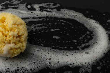 Natural sea sponge with soap foam on black background with copy space. Yellow sponge mockup, eco body care concept, eco friendly hygiene accessory mock up