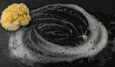 Natural sea sponge with soap foam on black background with copy space. Yellow sponge mockup, eco body care concept, eco friendly hygiene accessory mock up
