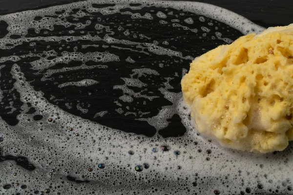 Natural sea sponge with soap foam on black background with copy space. Yellow sponge mockup, eco body care concept, eco friendly hygiene accessory mock up