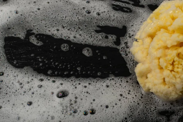 Natural sea sponge with soap foam on black background with copy space. Yellow sponge mockup, eco body care concept, eco friendly hygiene accessory mock up