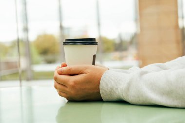 İki el kahve bardağını tutar. Kâğıt kahve fincanının üstünde sıcak eller, kafenin içinde fotokopi odası manzaralı ılık kupalar.